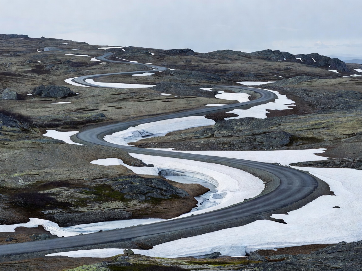Winding two-lane asphalt cutting across desolate rocky tundra and snowbanks in Sognefjellet
